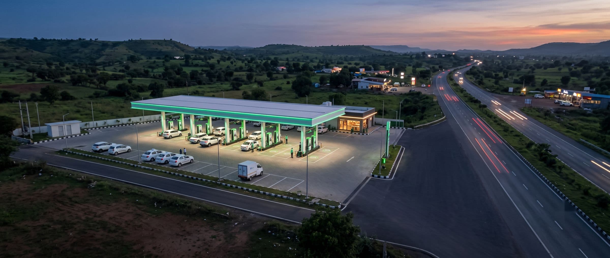 Aerial view of an EV charging plaza beside a highway at dusk